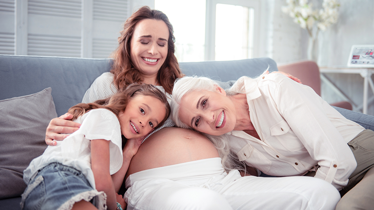 Woman laughing. Pregnant woman laughing while her daughter and mother listening to her tummy at home