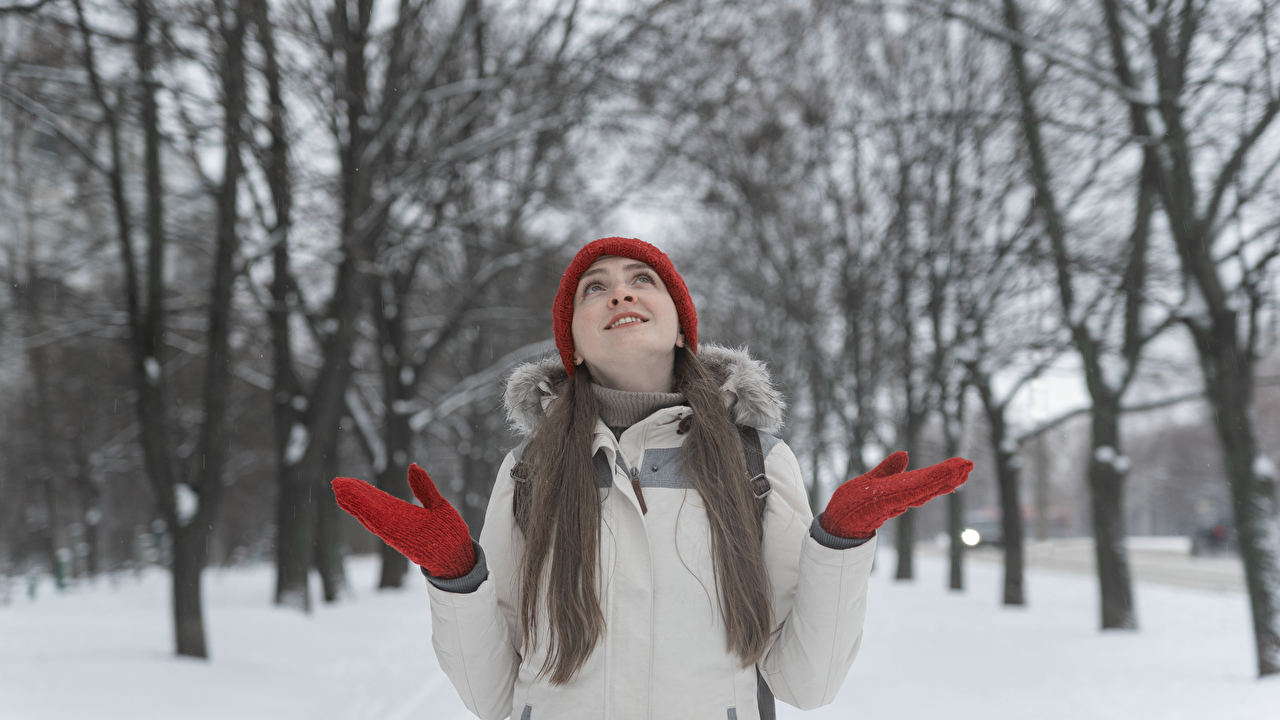Happy beautiful girl in knit red hat smiling while walking in winter park. Young woman on snowy park background